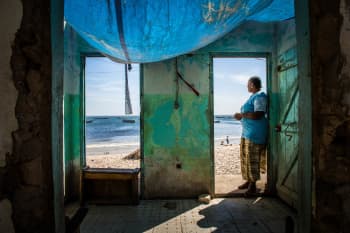 Mujer mirando el mar, varada junto a la puerta de una casa que está siendo destruida por la crecida de las aguas en Bargny, Senegal.