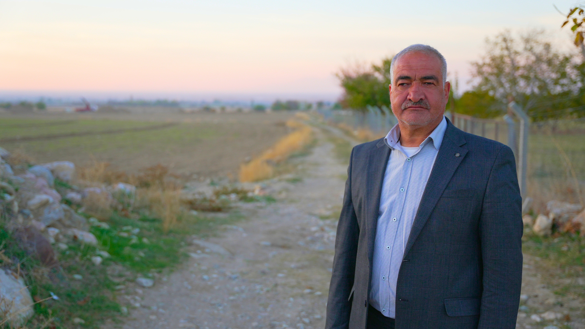 A close up photo of a Turkish farmer in front of his green fields